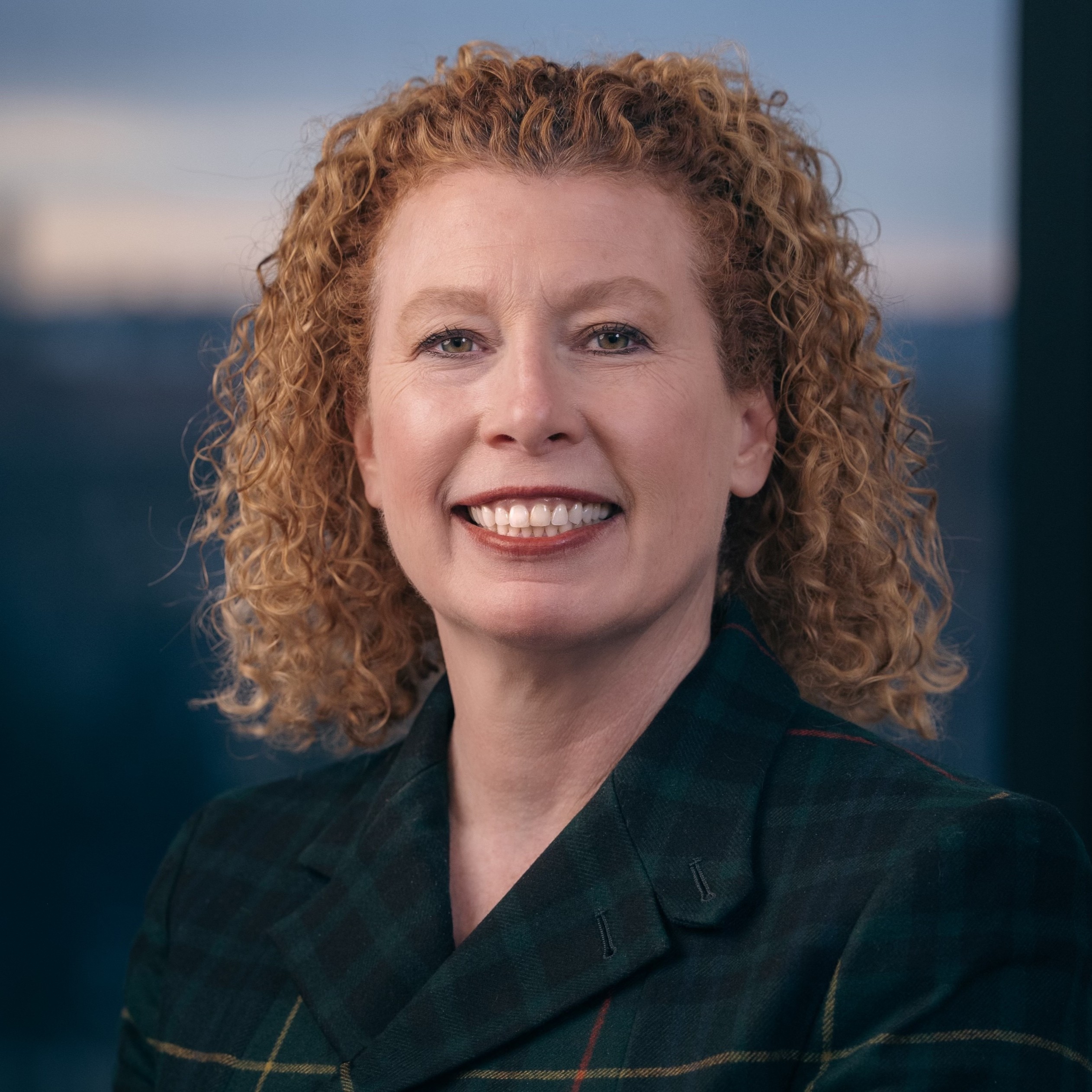 Colleen Fitzgerald with a sunset sky in the background smiles and looks at the camera.