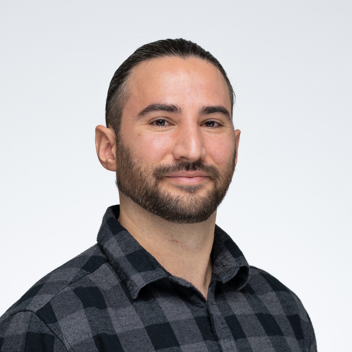 Connor Yiamkis in a green checkered shirt looking at the camera, against a white background.