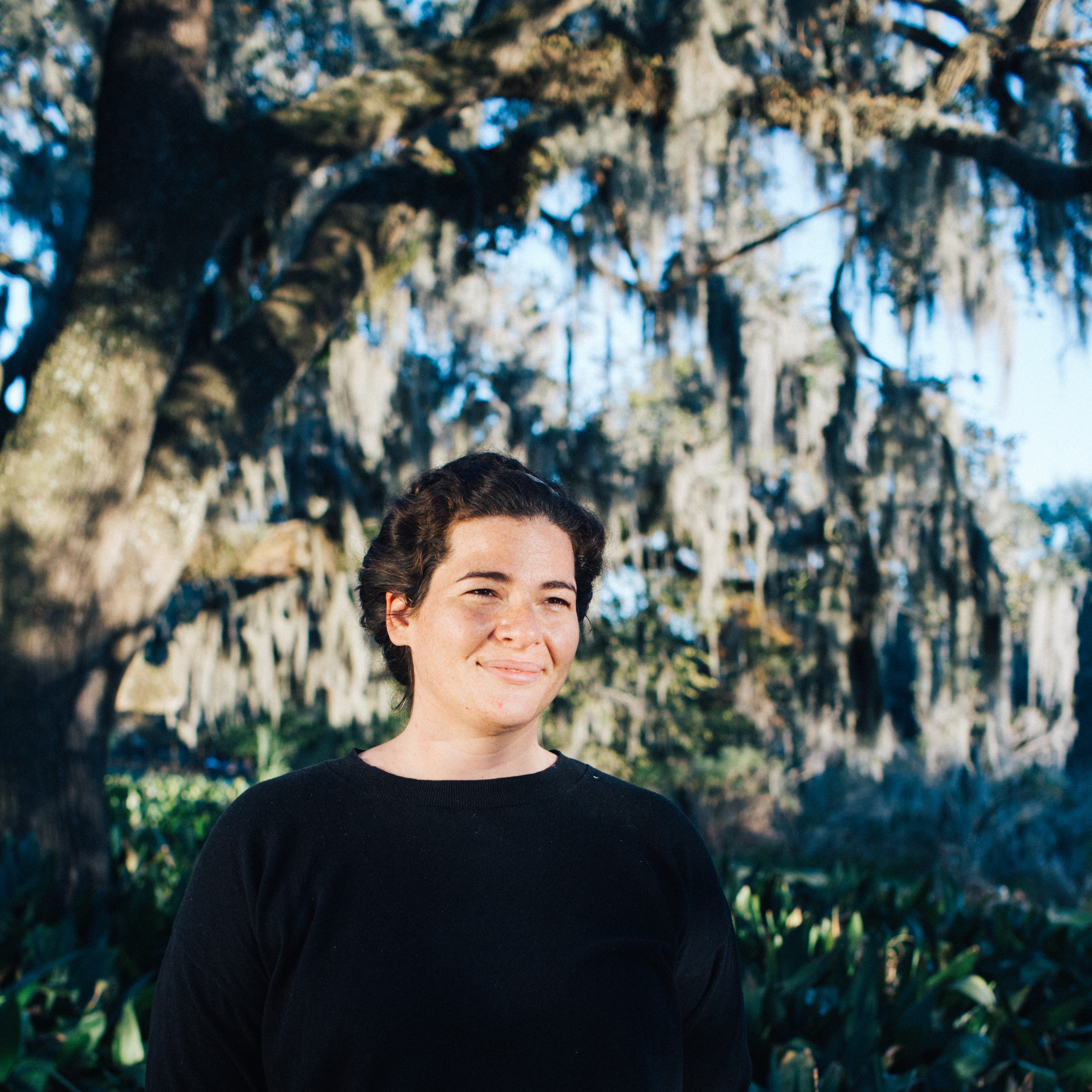 Hali Dardar smiling in the sunlight with a big tree in the background