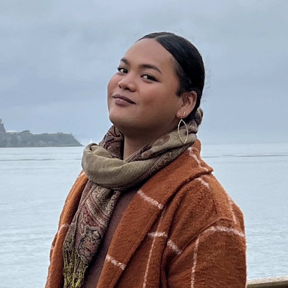 Måsi Santos by the ocean in an orange coat and scarf