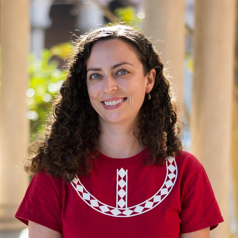 Jacqueline Brixey in a red shirt with white patterns smiling in the sunshine.