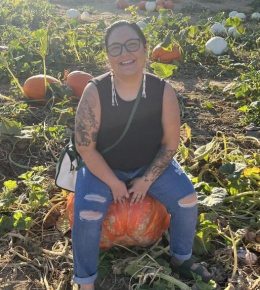 Stephanie Lumsden smiling and sitting on a pumpkin in a pumpkin patch