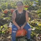 Stephanie Lumsden smiling and sitting on a pumpkin in a pumpkin patch